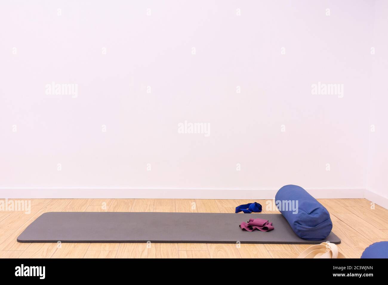 Pilates, exercise or yoga mat with a cushion, an elastic band and a belt, on the floor of a home or gym next to a white wall, with copy space Stock Photo