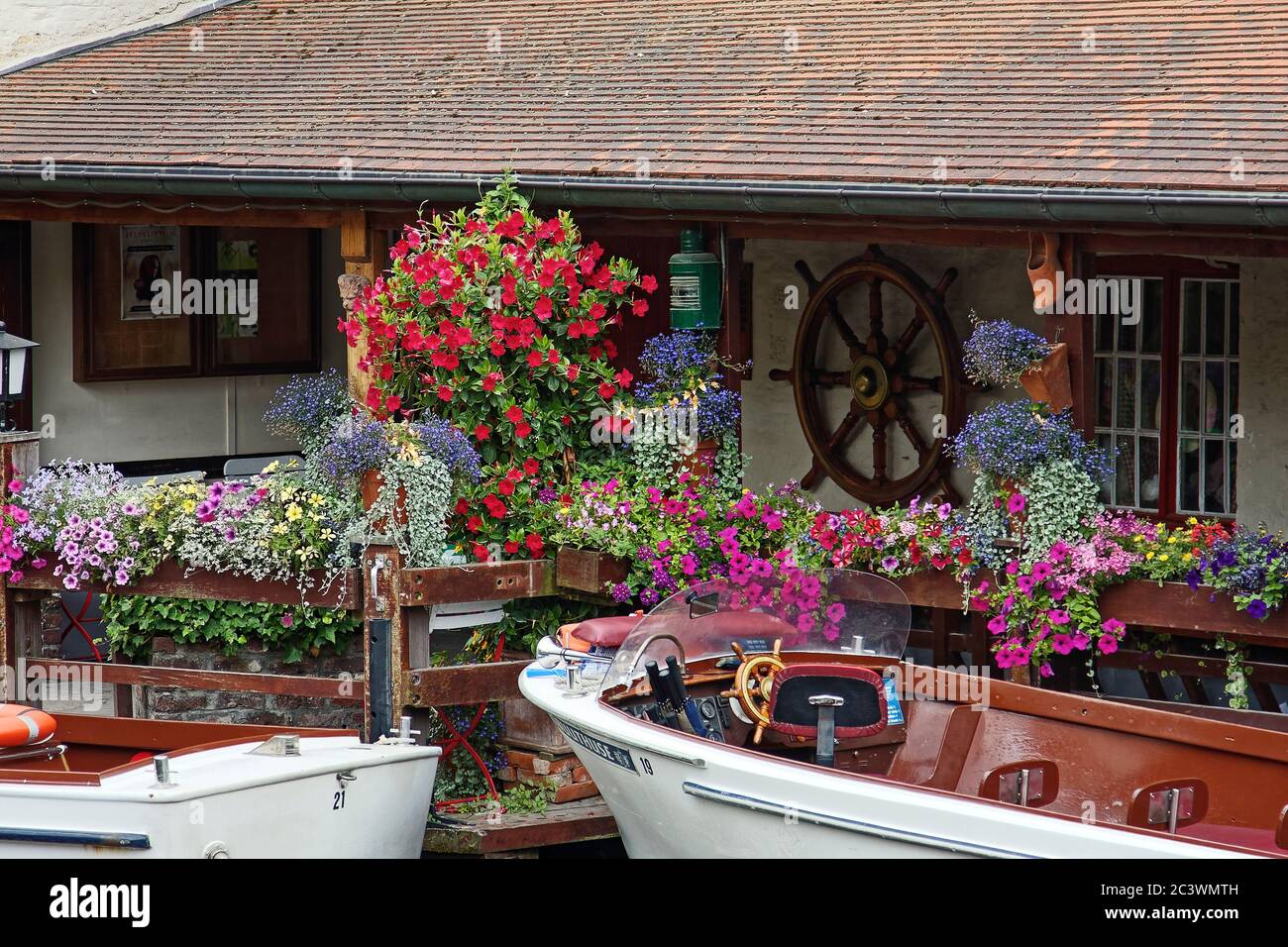 canal scene, small motor boats docked, colorful flowers, old building, ship's wheel decoration, marine, transportation, Europe, Bruges; Brugge; Belgiu Stock Photo