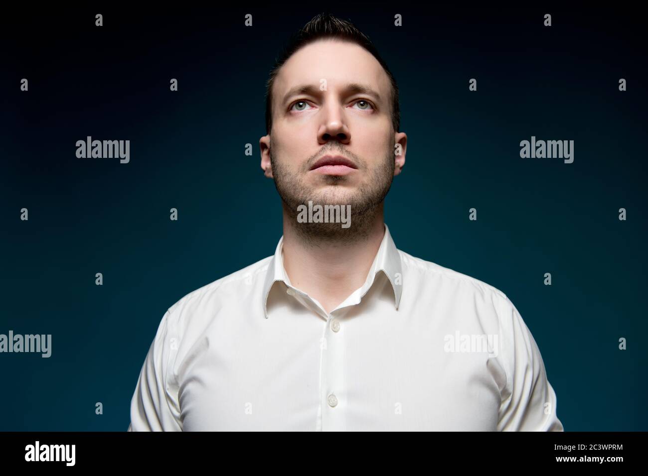 Young unshaven man in a white shirt looks into the void Stock Photo