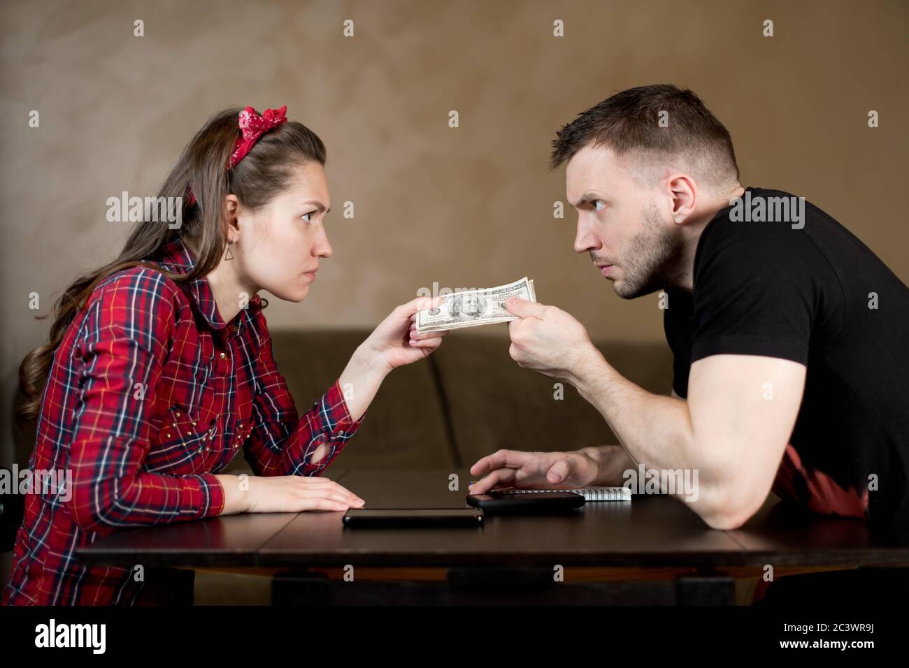 Husband and wife are pulling money at each other, angrily looking Stock Photo