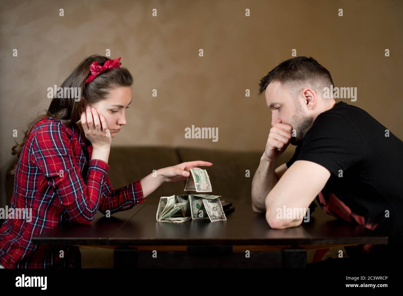 Husband and wife are sadly looking at the remaining money, sitting at a table Stock Photo
