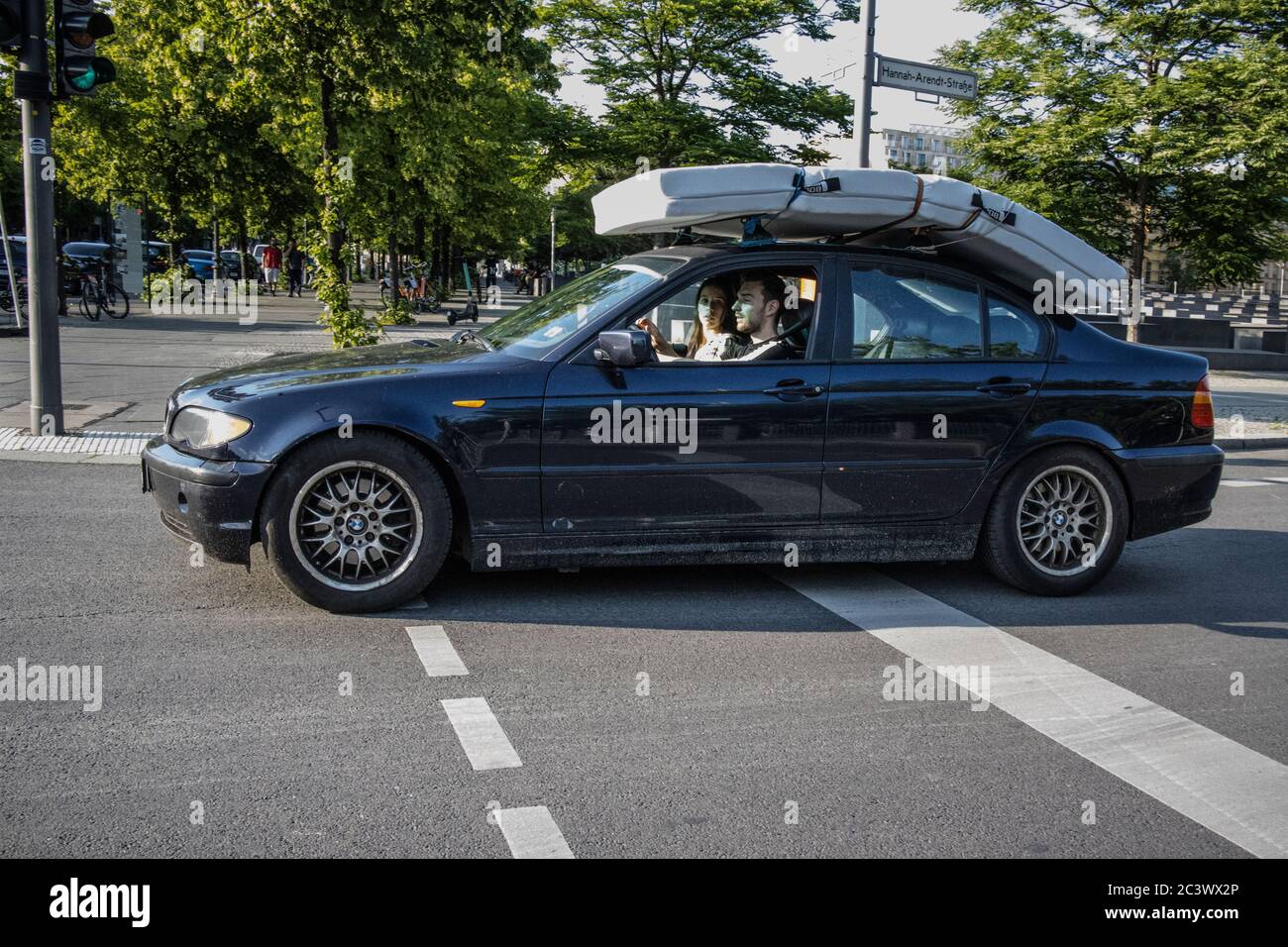 Young couple transport a bed mattress tied onto their BMW saloon car rooftop, Berlin, Germany Stock Photo