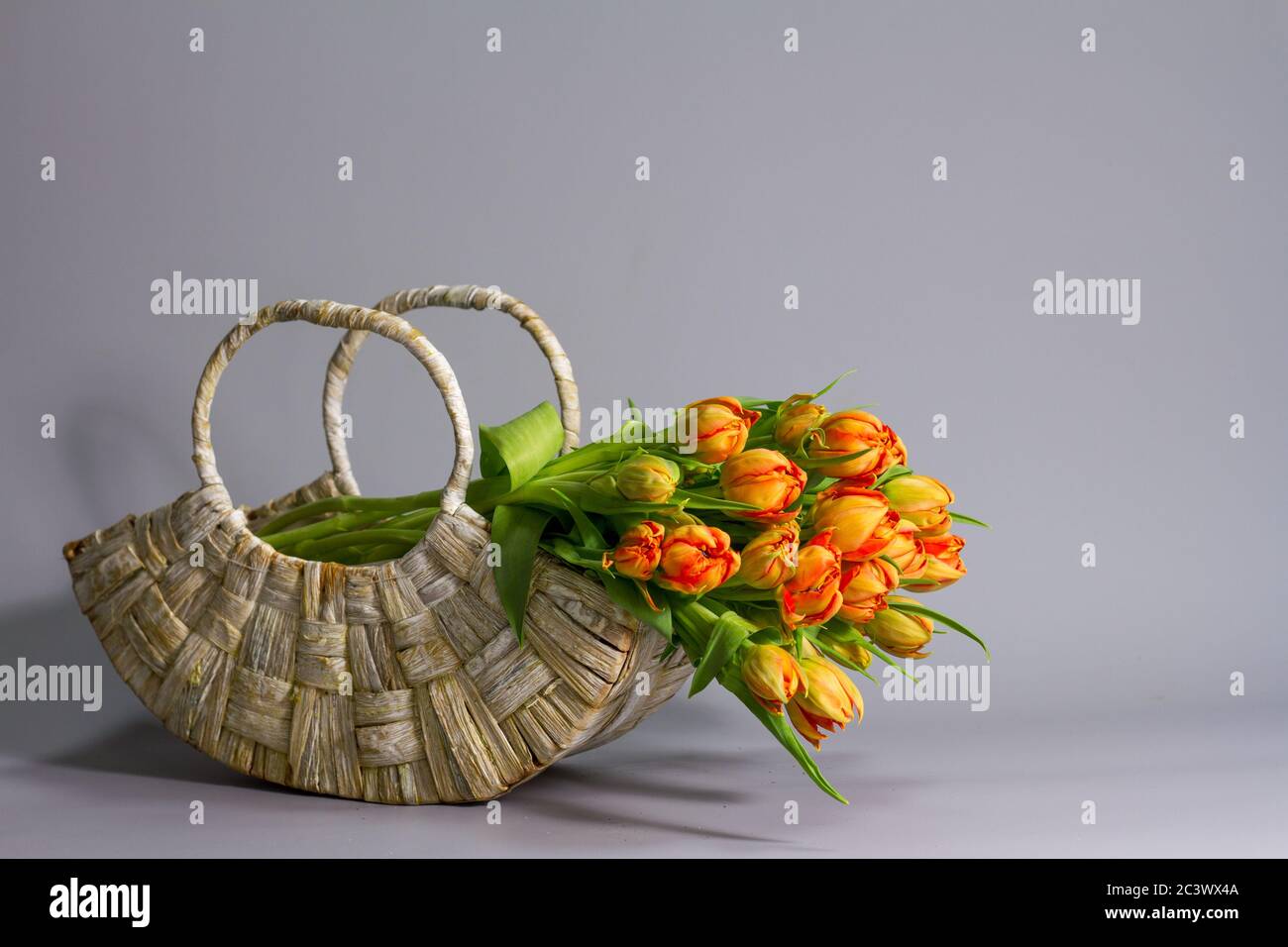 Straw basket with bouquet of fresh orange tulips on gray background, greeting or gift concept Stock Photo