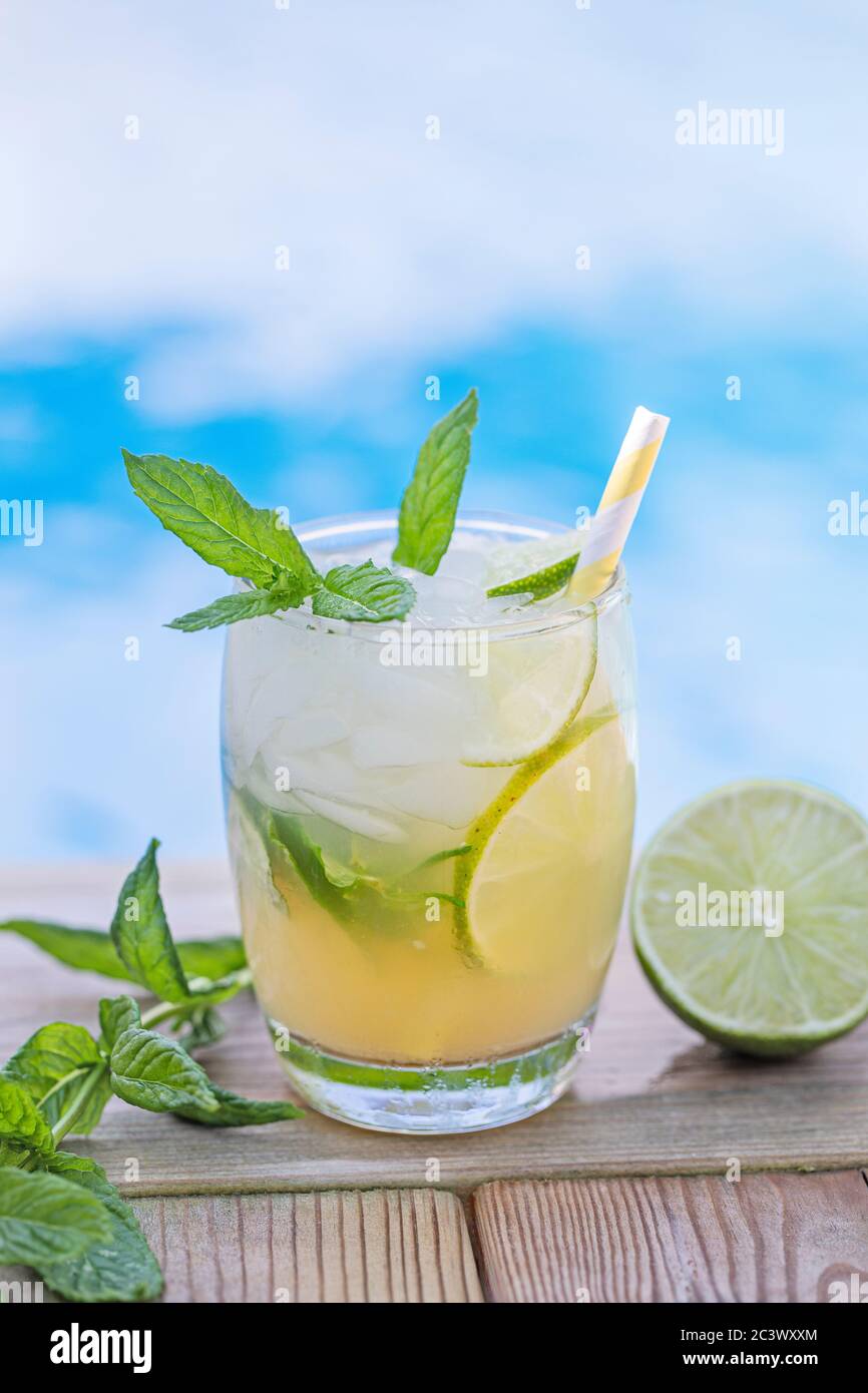 A fresh Mojito drink with mint leaves and lime and crushed ice, with blue pool water defocused in the background. Copy space room for text above the d Stock Photo