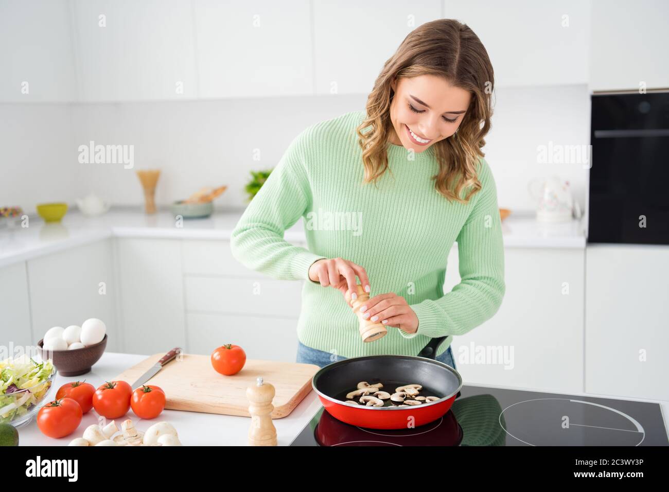 Portrait of her she nice attractive pretty focused cheerful cheery wavy-haired girl preparing delicious fresh hot domestic dish adding spice pepper in Stock Photo