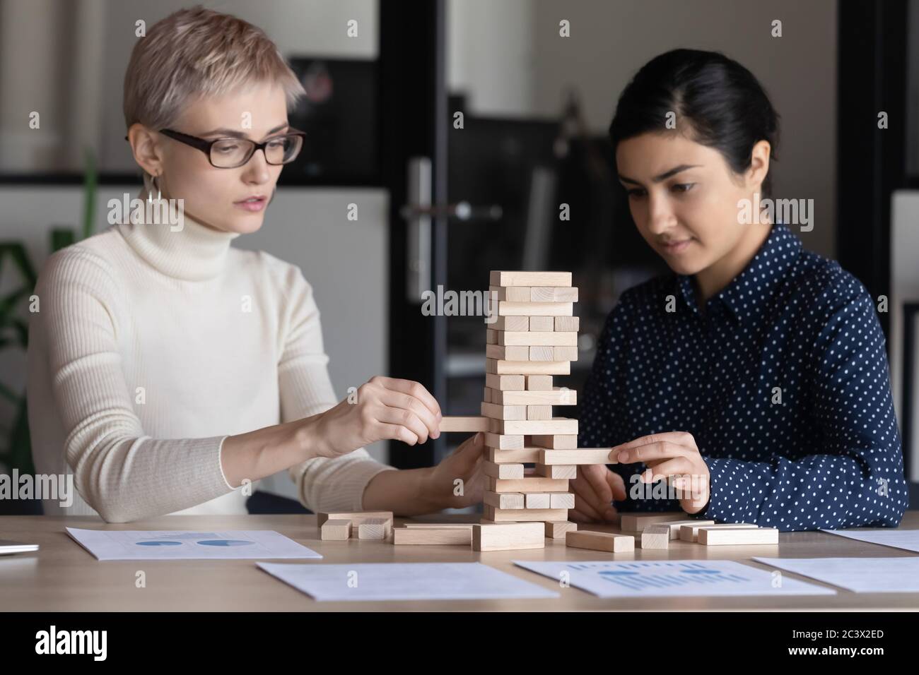 Two businesswomen build tower of wooden blocks play build game Stock Photo
