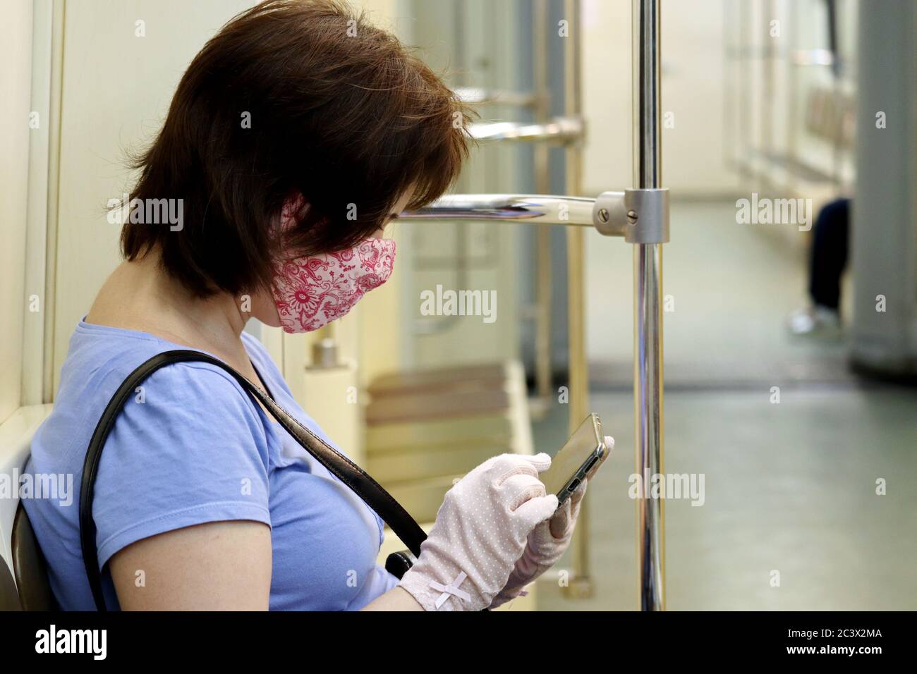 Woman in mask and protective gloves sitting in a metro train with smartphone. Interior of subway car during covid-19 coronavirus pandemic Stock Photo