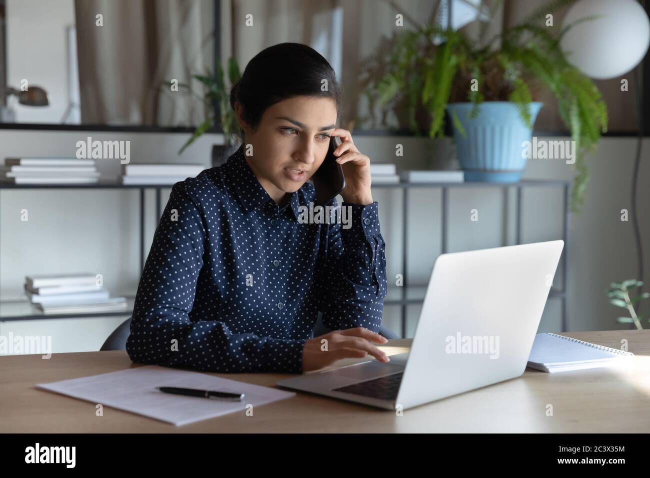 Indian businesswoman sit at workplace talking with client on phone Stock Photo