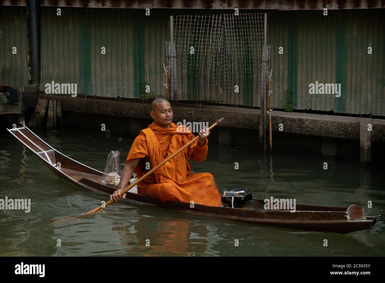 Bhudist monks and locals at Bangkok's floating market. A Monk paddling traditional boat moving left to right Stock Photo