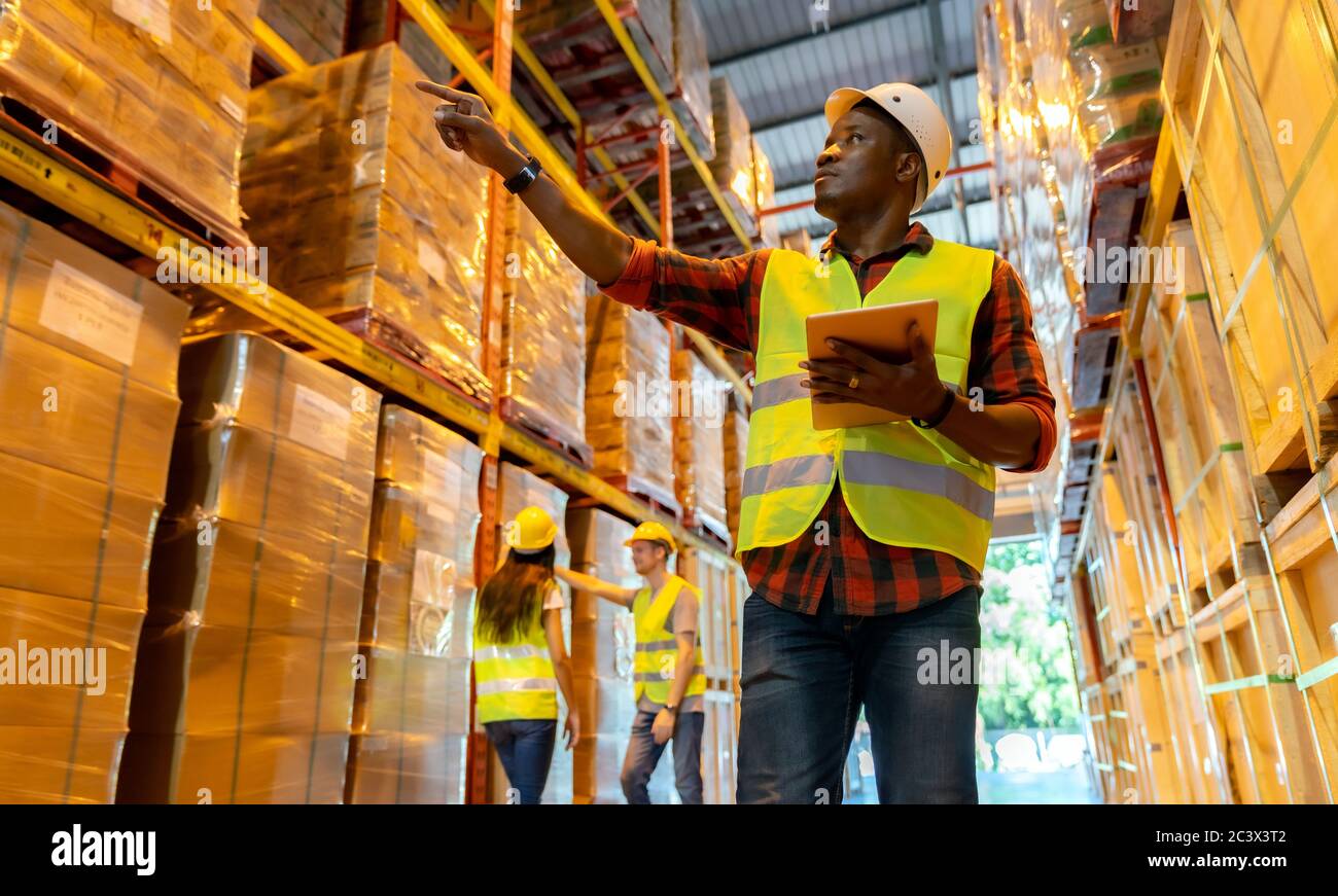 Portrait african black warehouse supervisor standing with digital tablet check stock in large warehouse distribution center with colleague worker in b Stock Photo