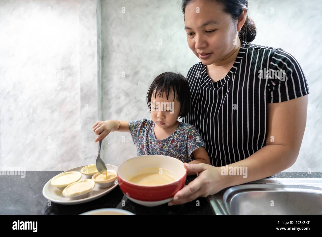 Asian girl cooking egg tart bakery with her mom, housework for child make executive function for kid. Houseworking food lifstyle and family concept. Stock Photo