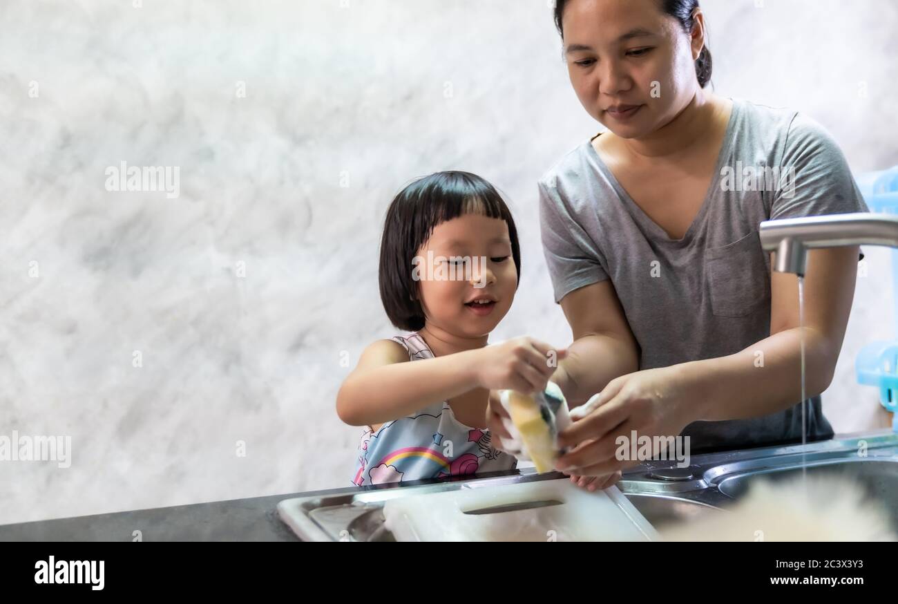 Asian girl washing dish and tableware with her mom, housework for child make executive function for kid. Houseworking for kid lifstyle and family conc Stock Photo