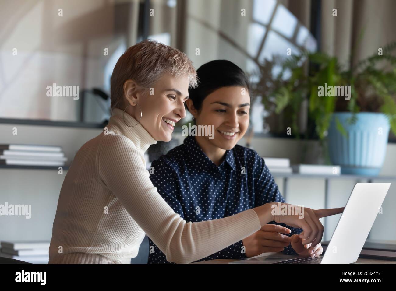 Multiethnic female colleague international department members working together using laptop Stock Photo