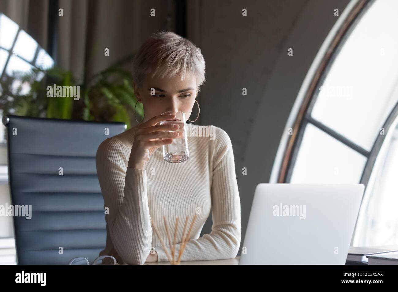 Serious businesswoman drinking water looking at laptop screen at workplace Stock Photo