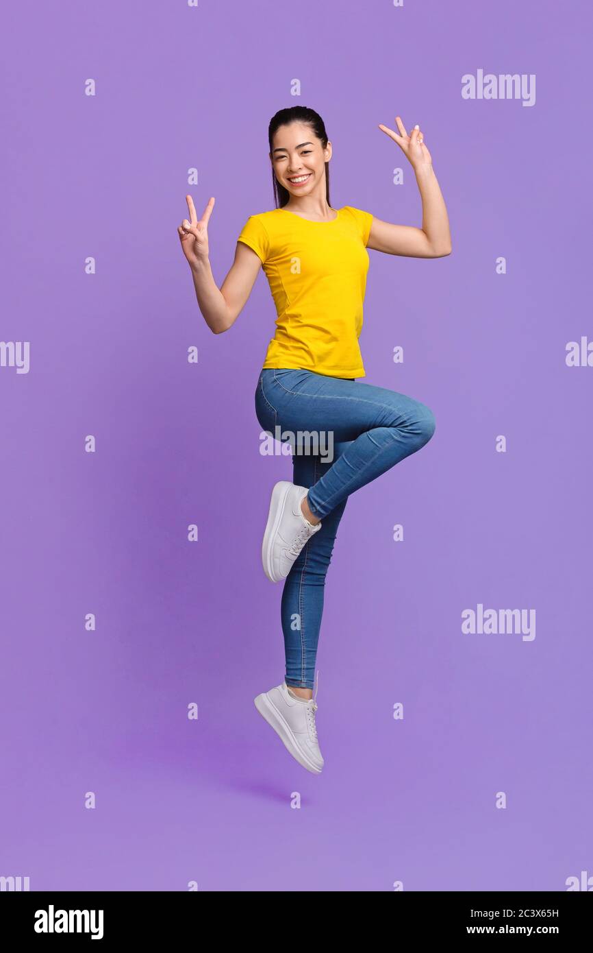 Carefree Mood. Cheerful Asian Girl Jumping In Air And Showing Peace ...