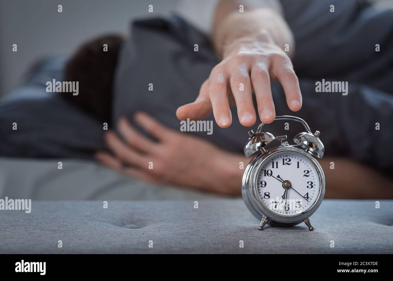 Man Turning Off AlarmClock Lying In Bed At Home Stock Photo Alamy