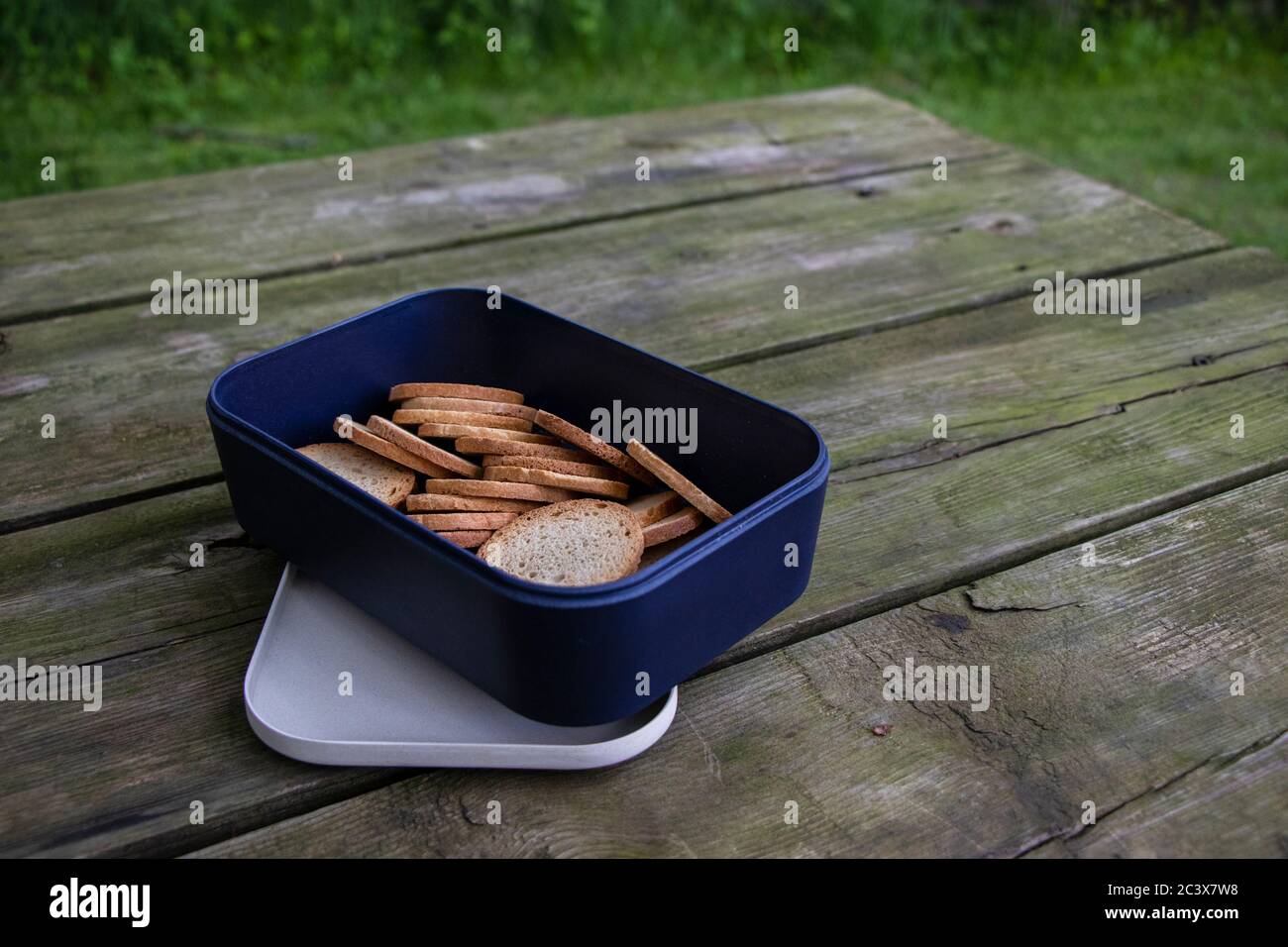 Reusable opened Bento Box container on a rustic wooden picnic table with crackers, view from above, Camping Outdoors Stock Photo