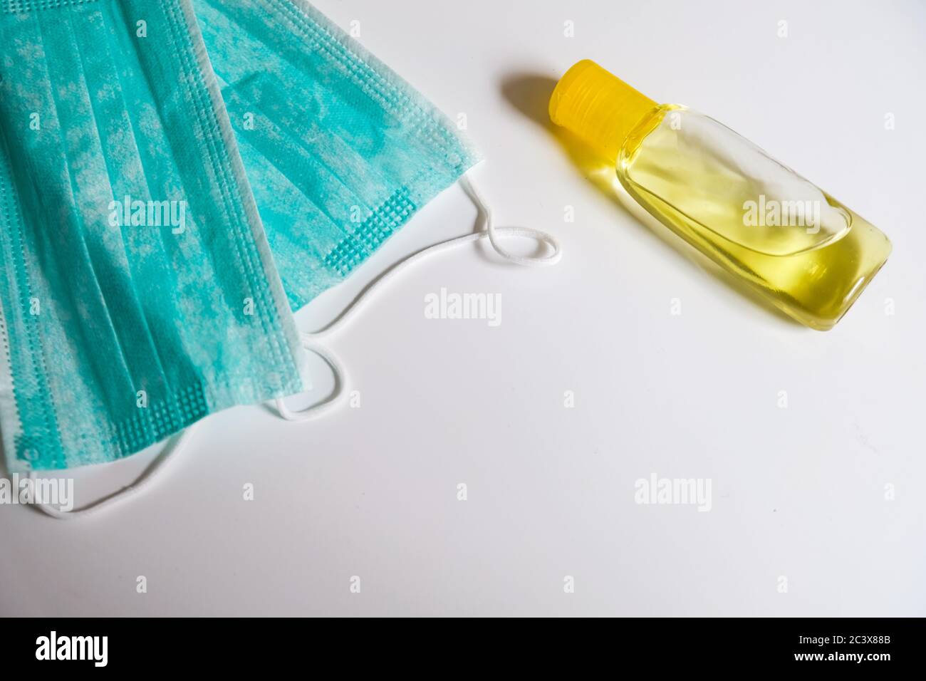 Two simple blue face masks and yellow bottle of hand sanitizer laying on a white desk. Empty space for copy. Virus spreading prevention Stock Photo