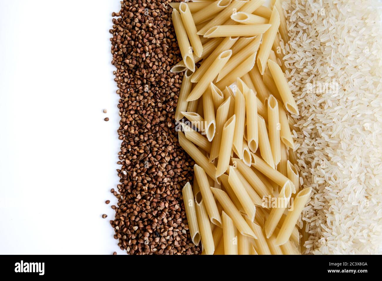 Whole grains on white table. Raw buckwheat, pasta, rice. Empty space