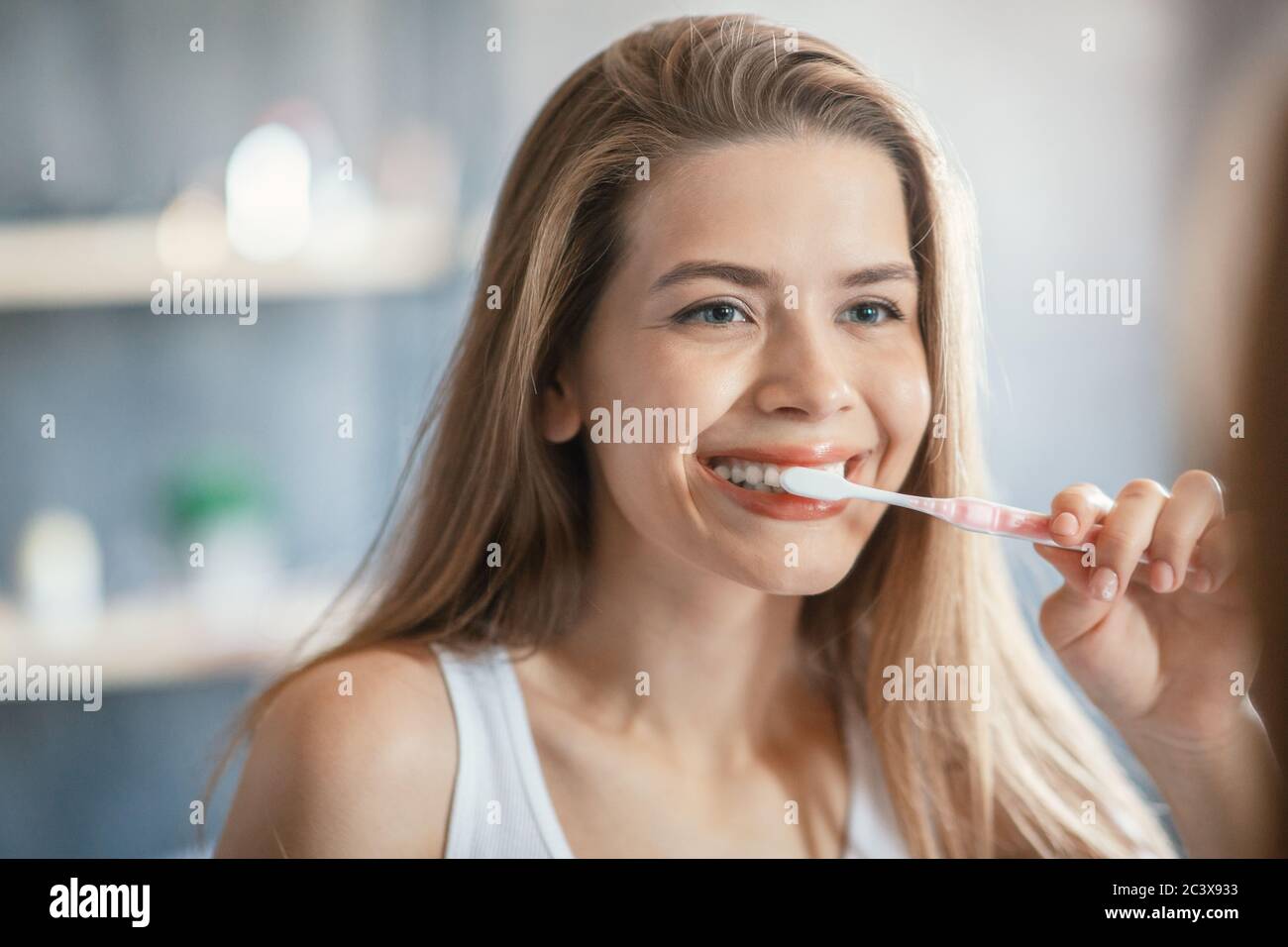 Young girl with beautiful smile brushing her teeth in front of mirror