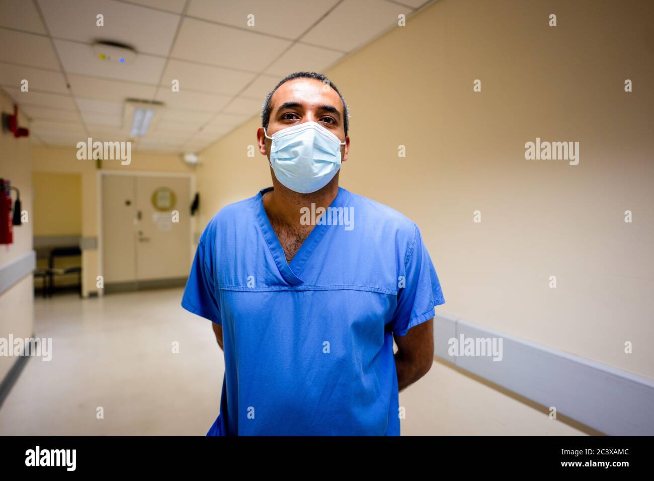 A doctor wearing a protective mask poses for a portrait on a ward in
