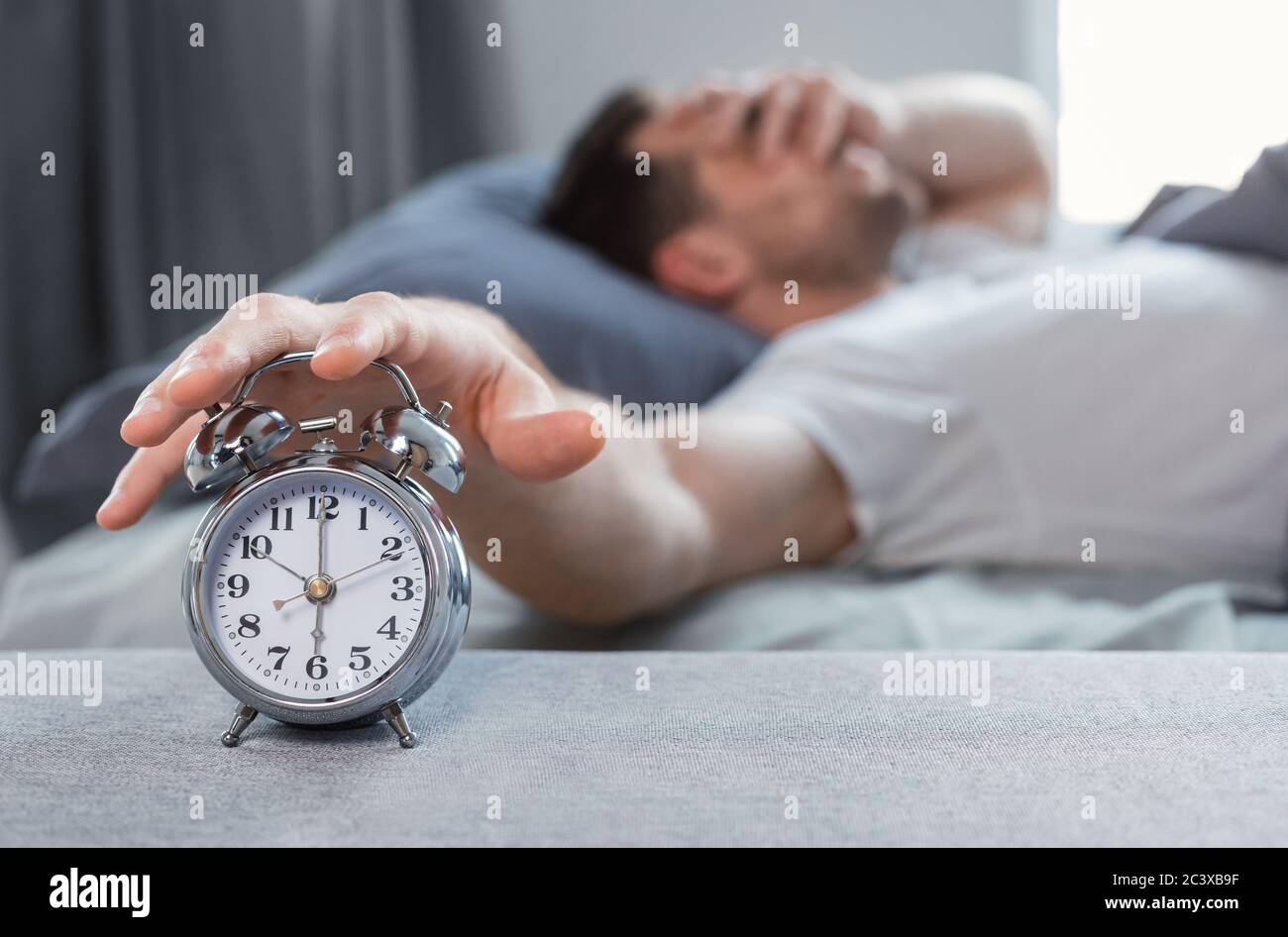 Sleepy Man Turning Off AlarmClock Waking Up In Bed Indoors Stock Photo