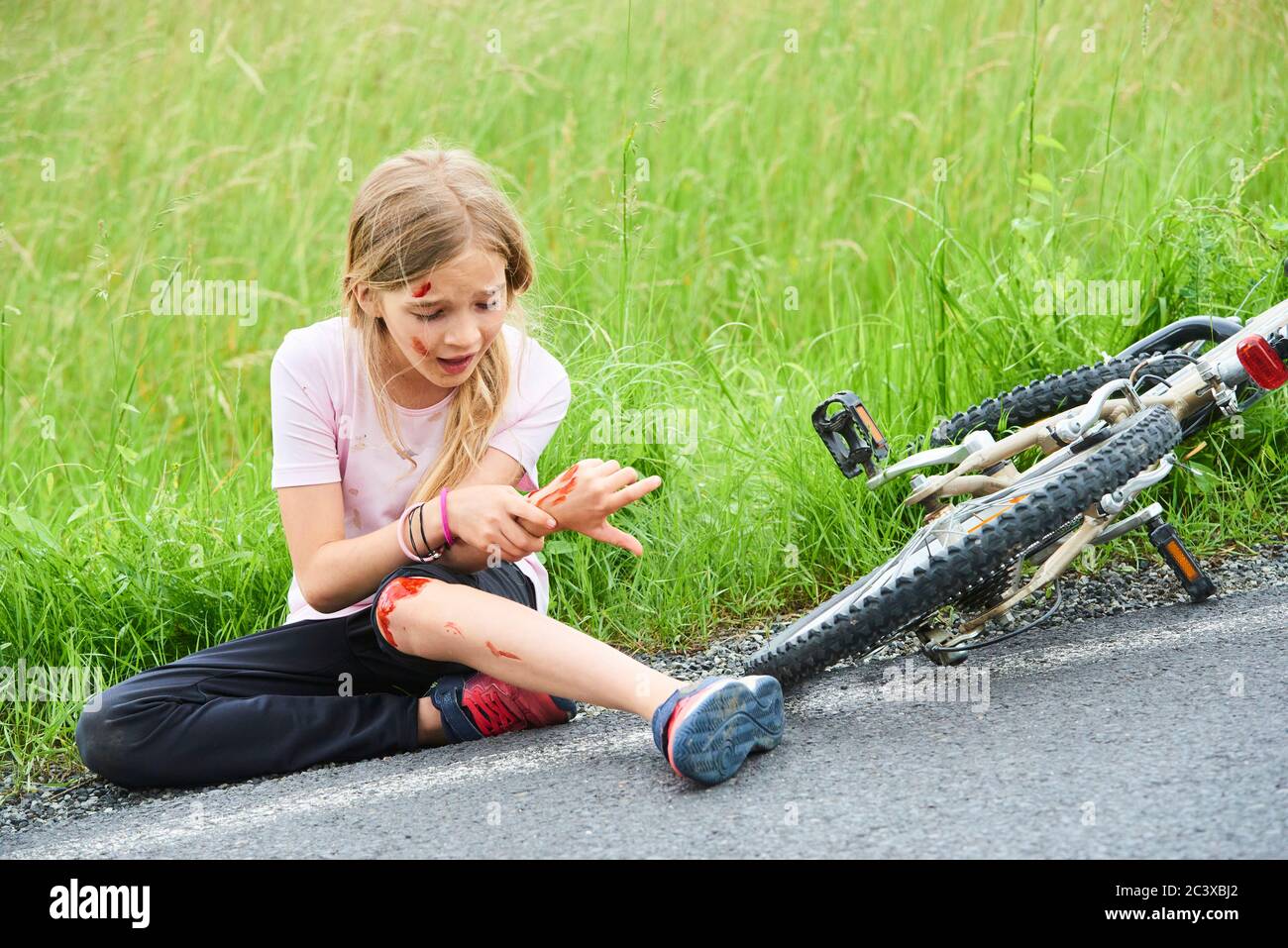 Sad crying little child girl fell from the bike in the summer park