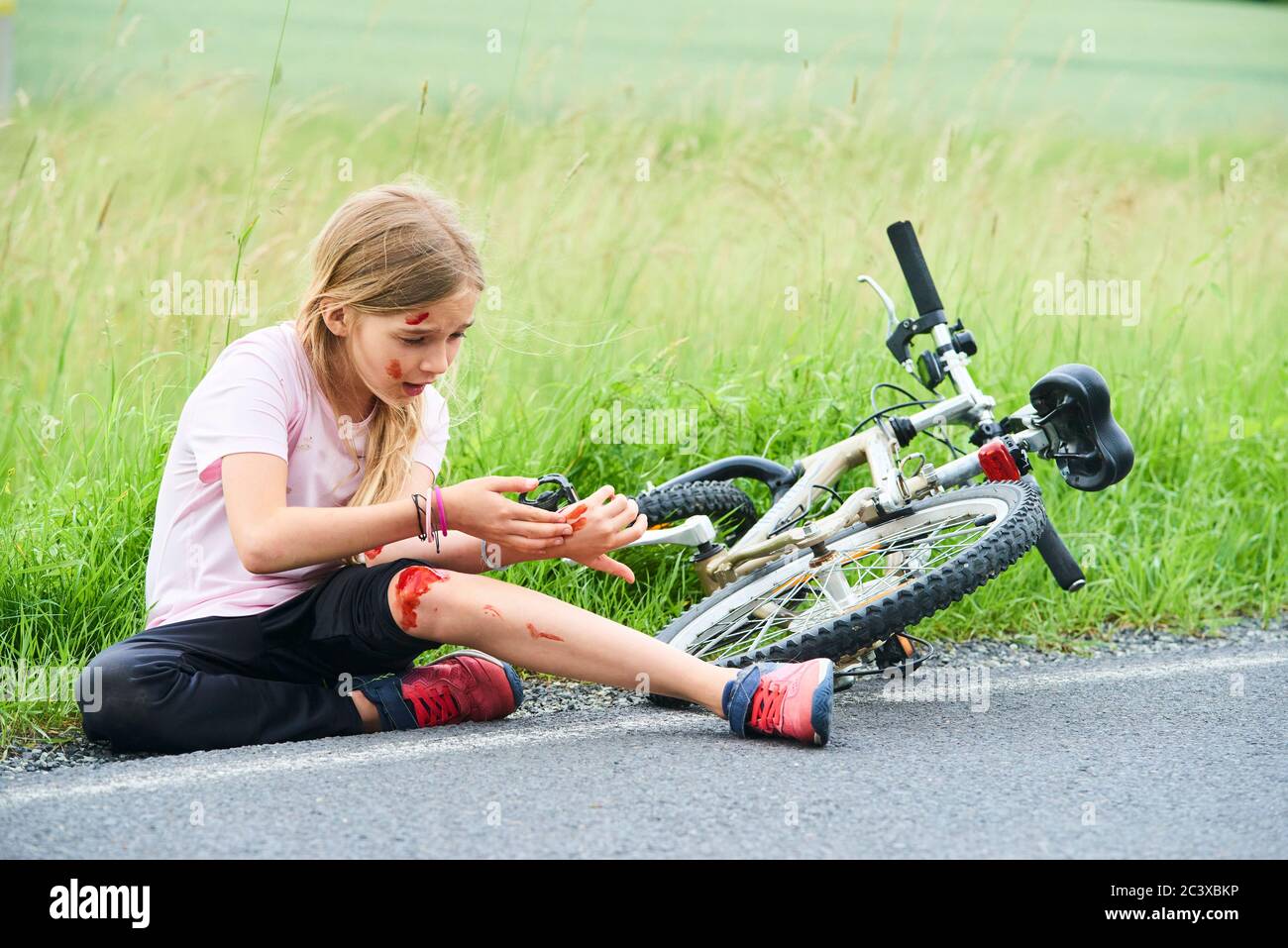 Sad crying little child girl fell from the bike in the summer park