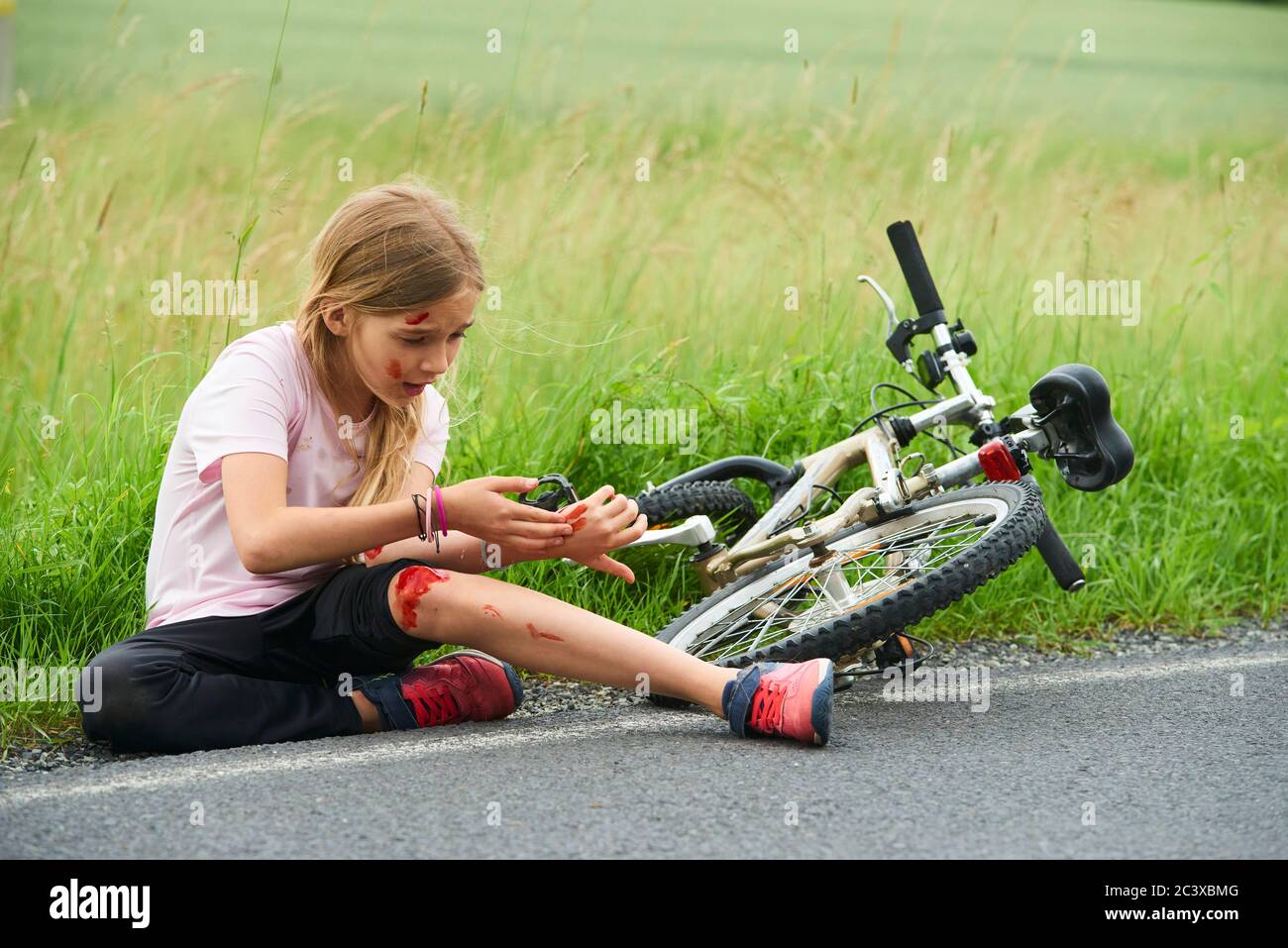 Sad crying little child girl fell from the bike in the summer park