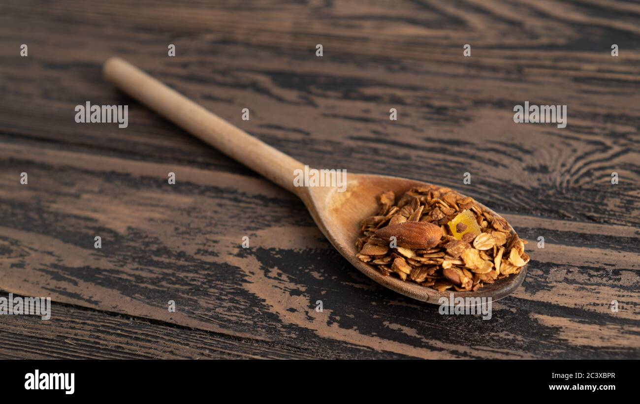 one standalone wooden spoon serving of granola with nuts. blurred wooden background. place for text. small portion Stock Photo