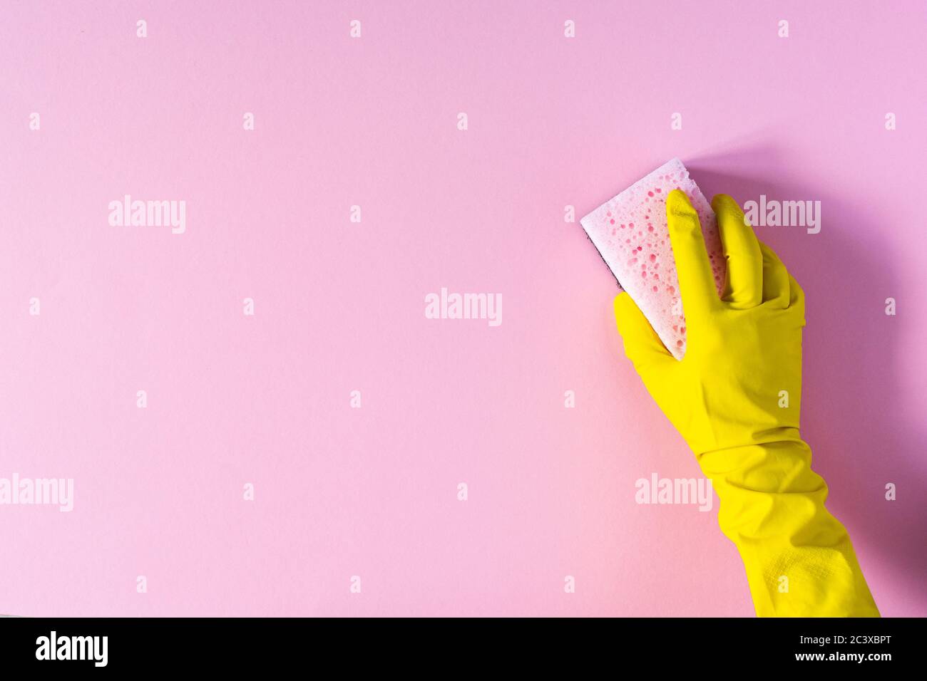 Hand in a yellow rubber glove with a cleaning sponge on a pink ...