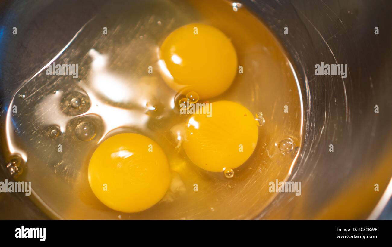 Yellow eggs on metallic bowl. Three chicken egg yolks. Preparation for scrambled eggs in a metal bowl. Cooking eggs Stock Photo