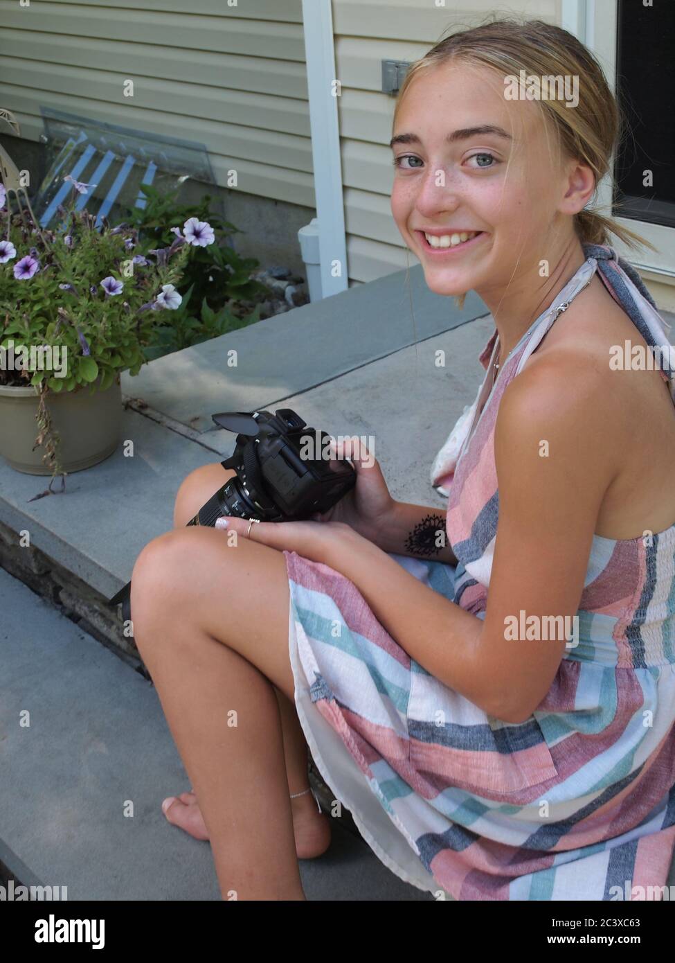 Pre teen girl smiling a camera in a summery dress while she holds an  expensive digital camera Stock Photo - Alamy