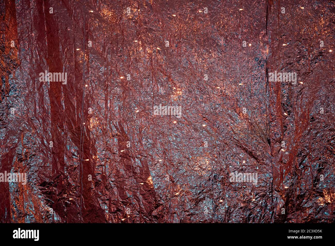 Red golden metallic rumpled foil backdrop with shiny lights.  Glitter texture of folded metallic fabric. Bright shimmer Christmas glowing background. Stock Photo