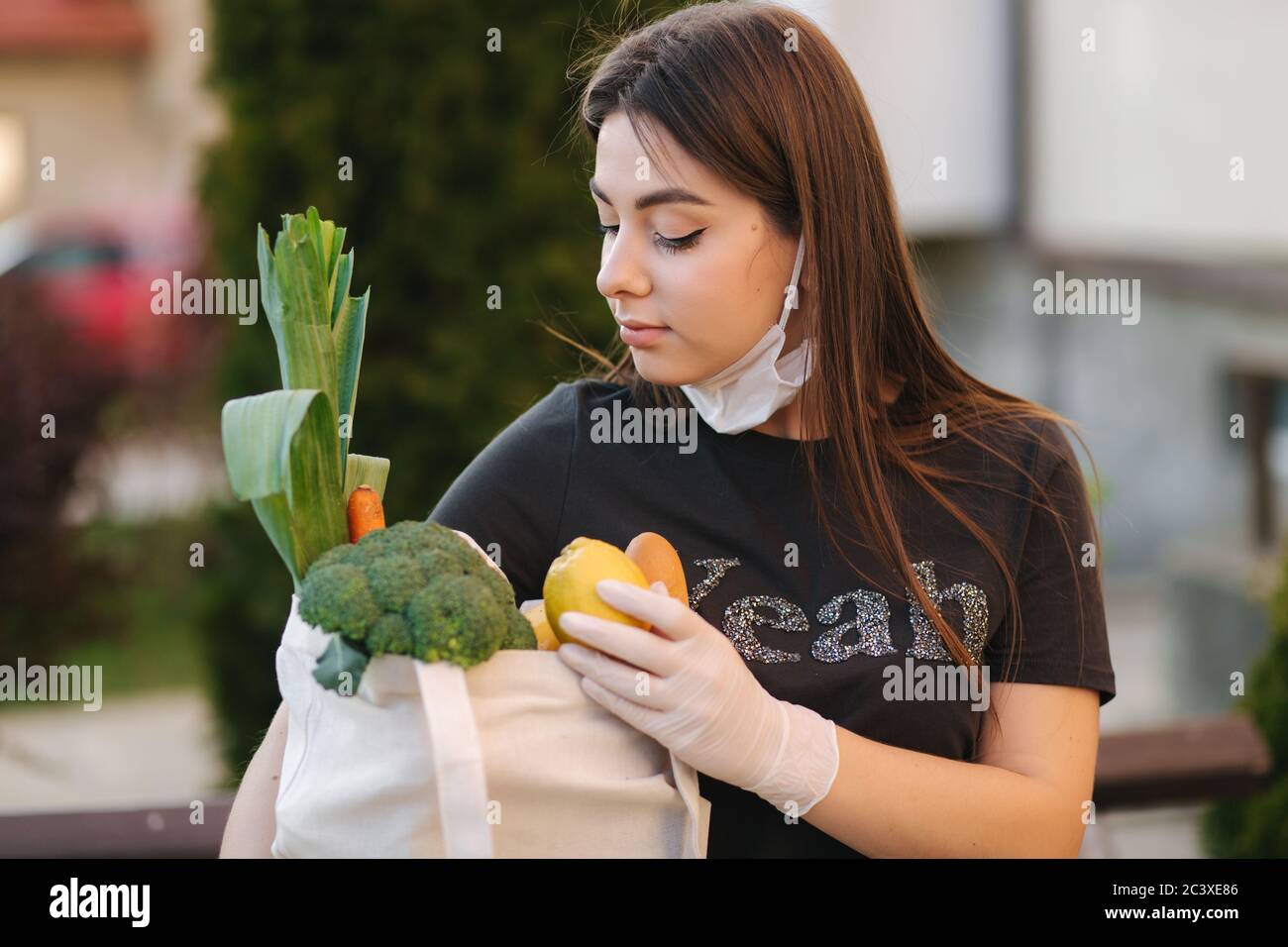 Young woman in mask and gloves hold bag with fresh food, vegetables ...