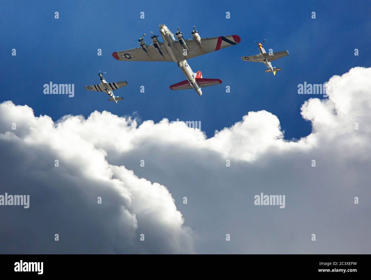 A B-17 'Flying Fortress' bomber is escorted by two P-51 Mustang fighters above dramatic clouds in a deep blue sky. Stock Photo