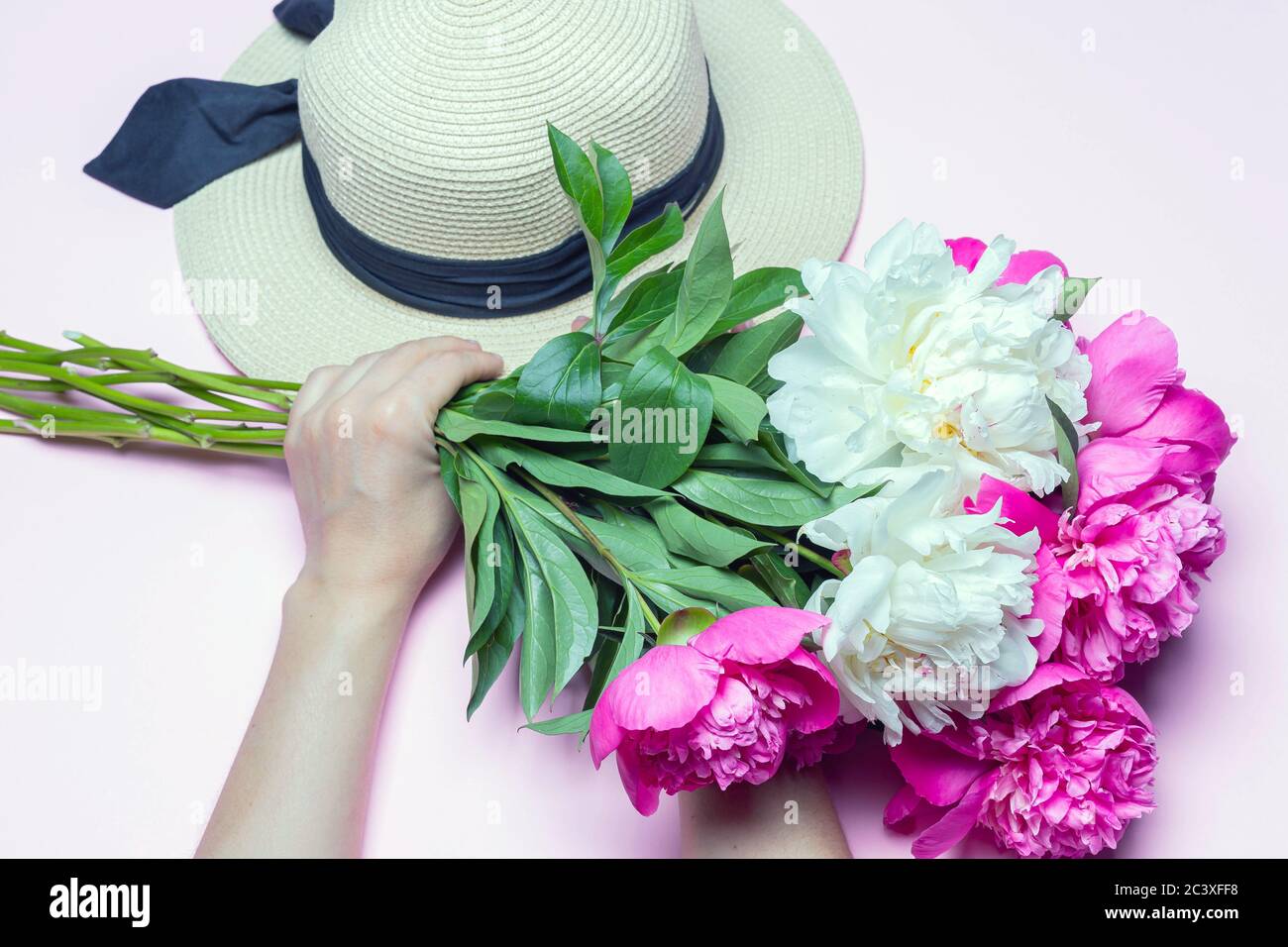 Mix peonies bouquet and straw hat in female hands isolated on pink ...