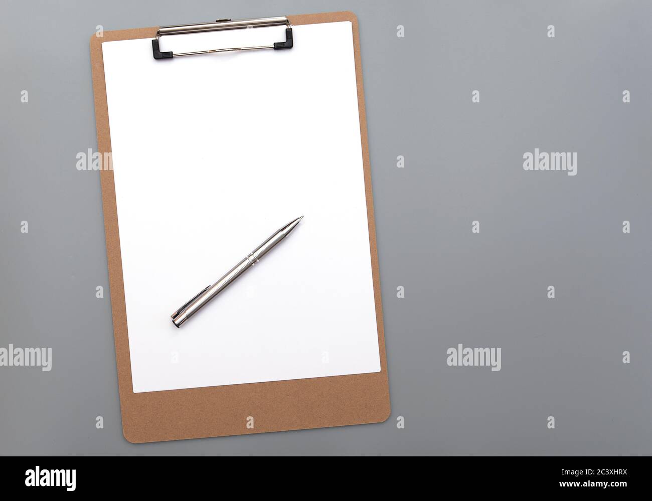 Paper clipboard with clean white blank paper and silver iron pen on gray background, top view Stock Photo