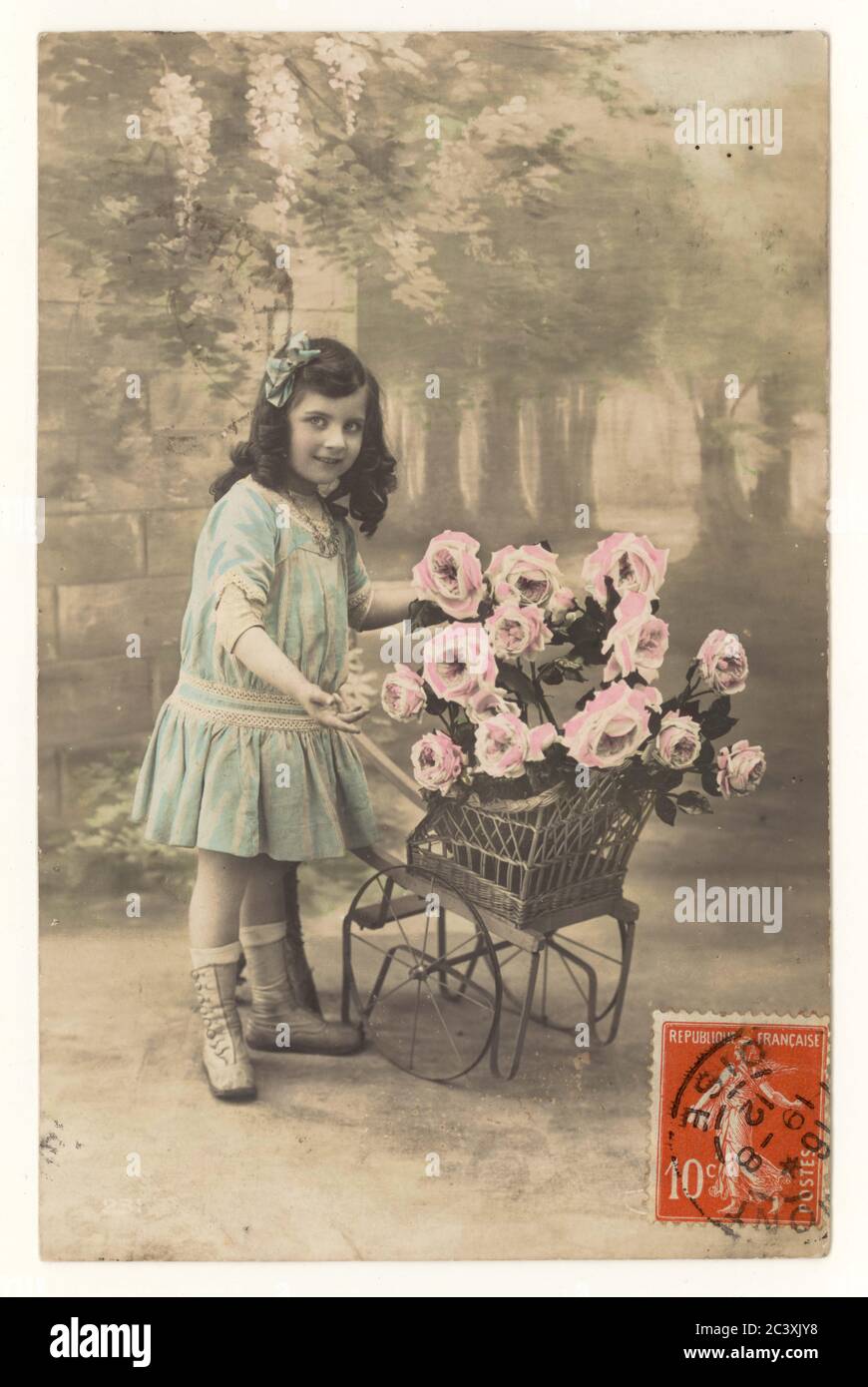 Early 1900's sentimental French postcard of young girl with wheelbarrow full of roses, postmarked 19 Aug 1912, France Stock Photo