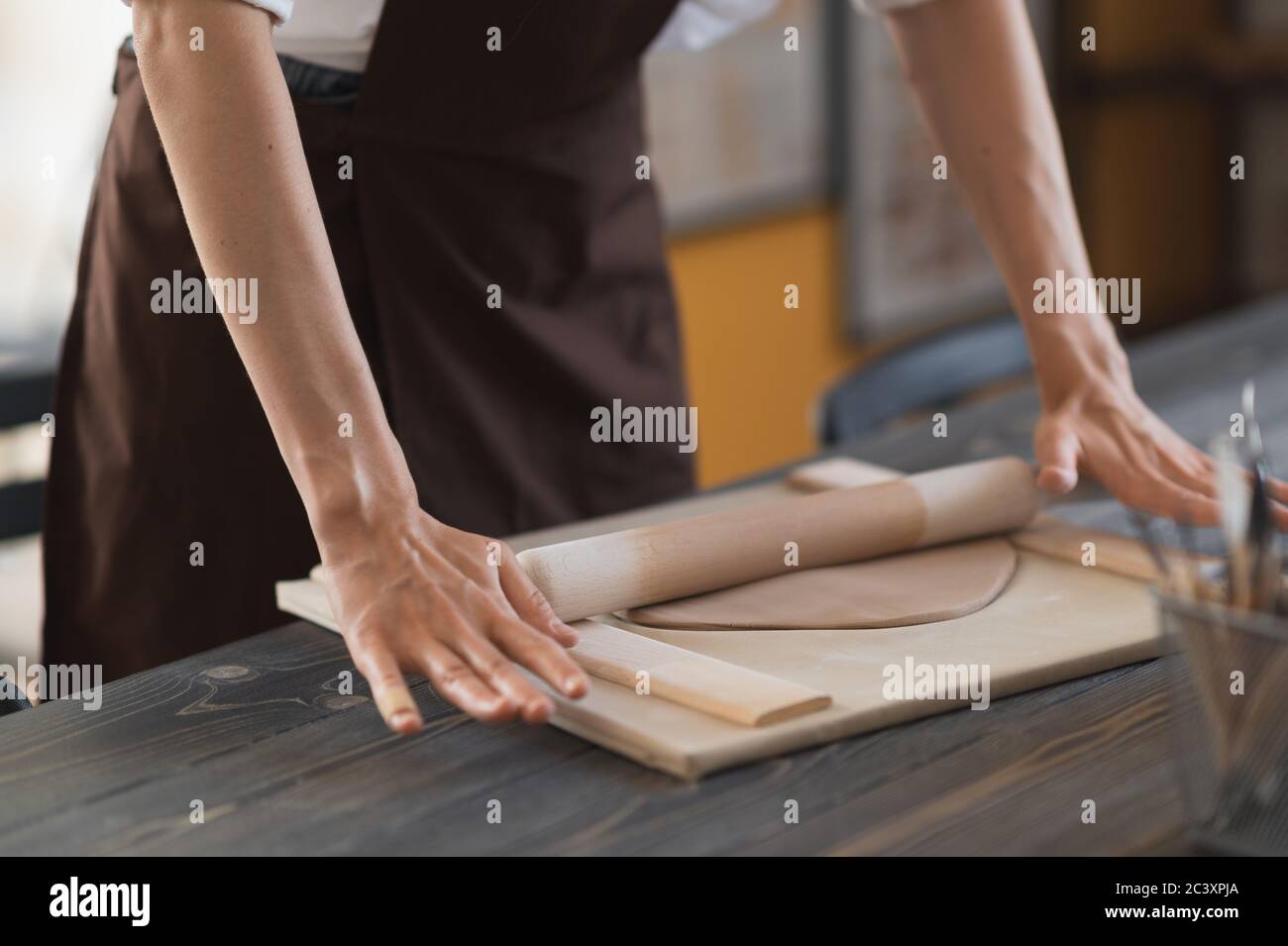 Female hands flatting piece of clay lying on fabric using wooden