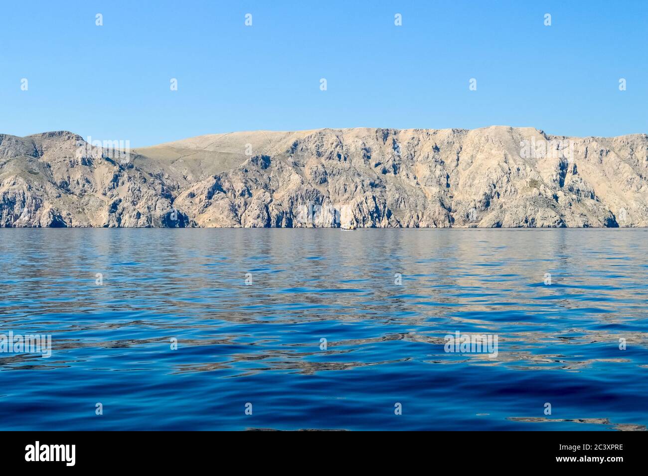 Barren rocks in the rippling sea with clear blue sky Stock Photo