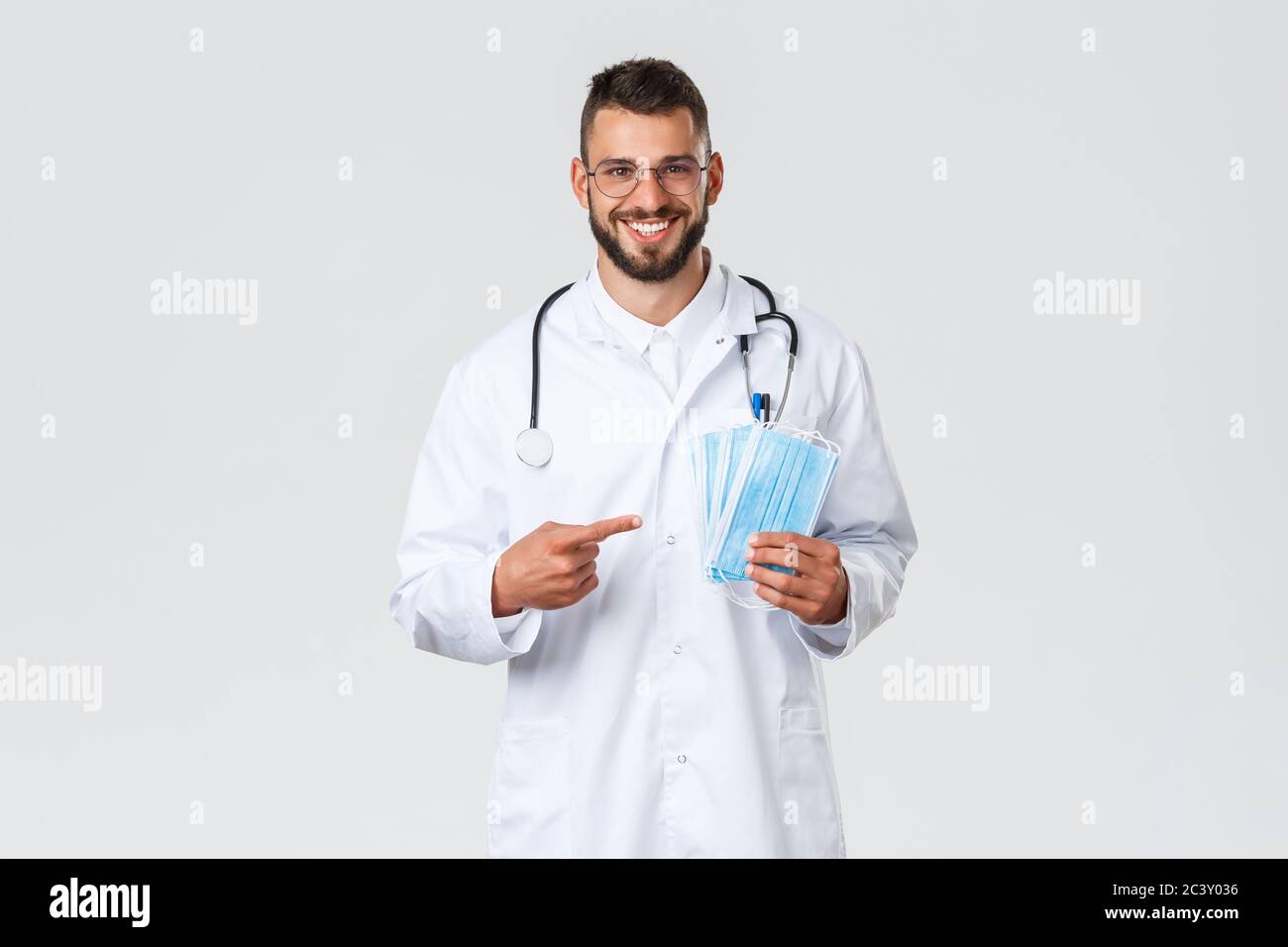 Healthcare workers, medical insurance, pandemic and covid-19 concept. Cheerful, smiling handsome doctor recommend using medical masks, physician in Stock Photo