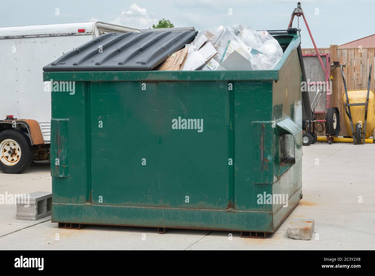 Large metal recycling bin filled to capacity with items including cardboard, plastic and glass