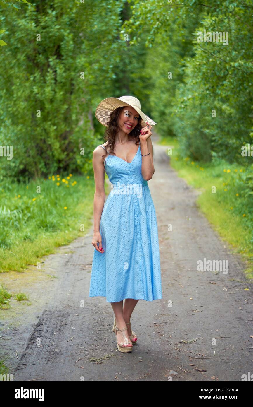 beautiful girl in a straw hat and blue dress on the road in the Park ...