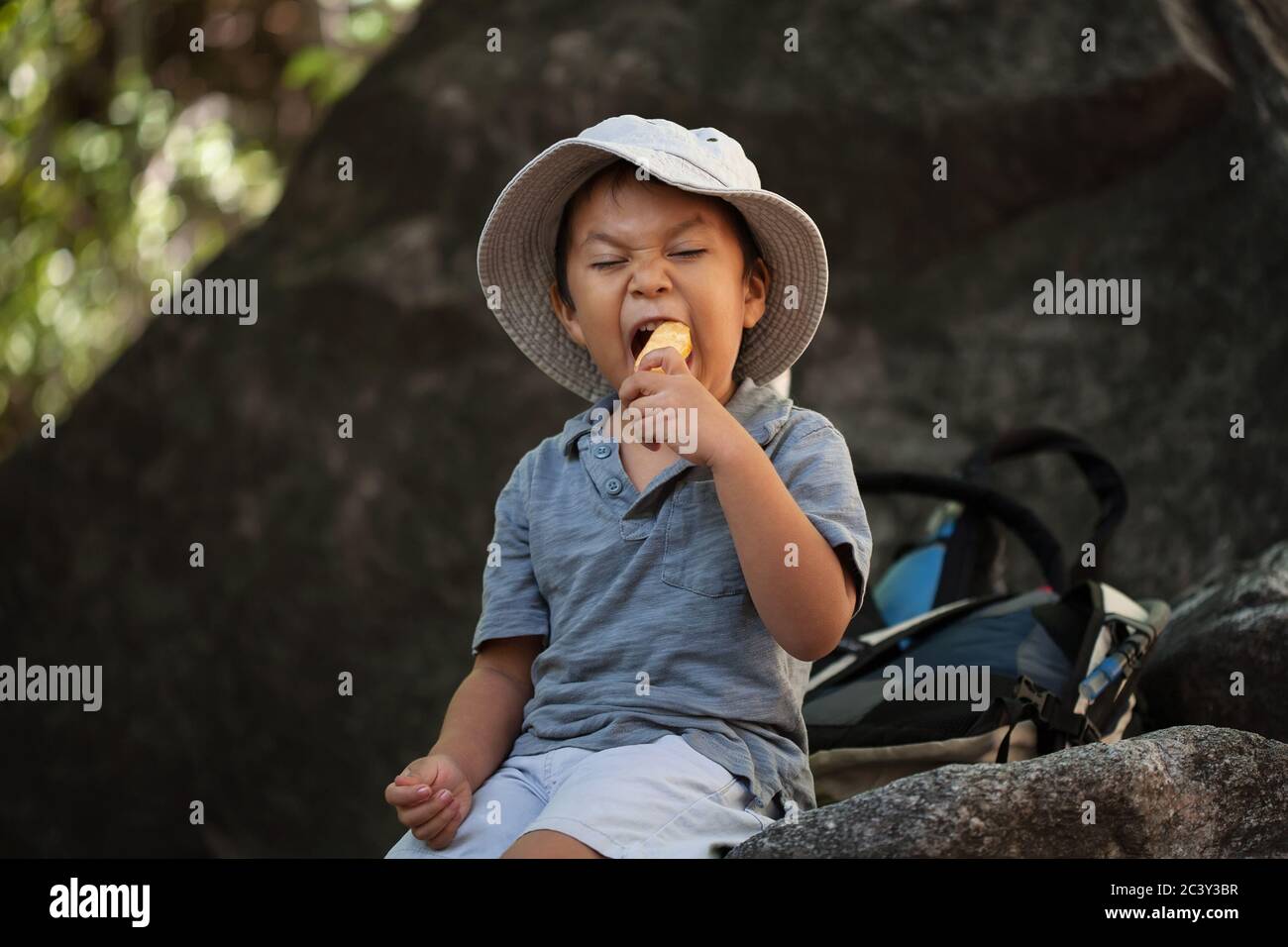 Eating healthy snacks, a young boy is taking a bite out of a apple while resting during a hike. Stock Photo
