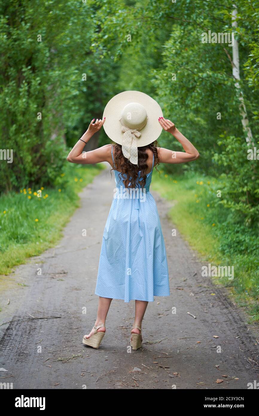 beautiful girl in a straw hat and blue dress on the road in the Park ...