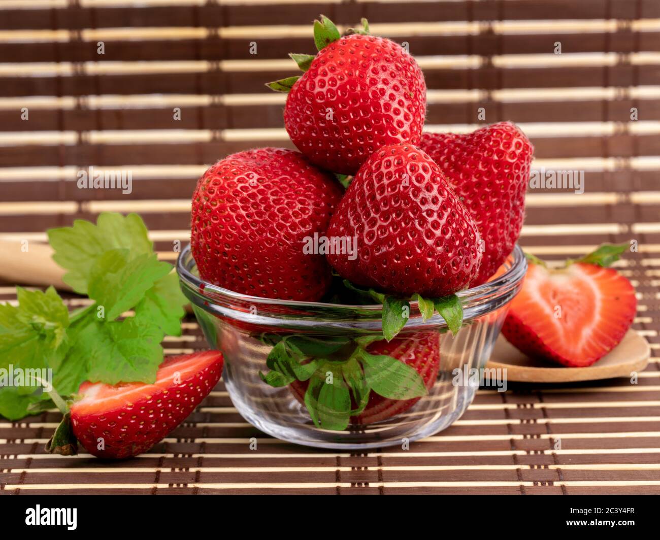 large ripe red strawberries whole and cut up in a small glass bowl on a ...