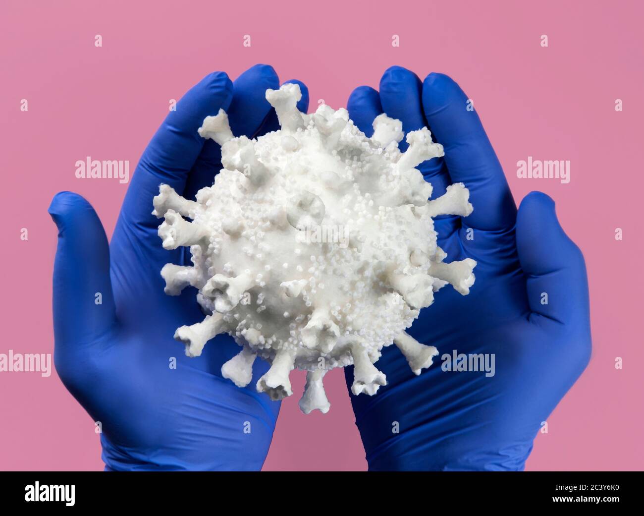 Hands in blue latex gloves holding Coronavirus model Stock Photo