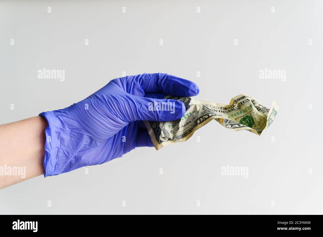 Studio shot of hand in latex glove holding crumpled dollar bill Stock Photo