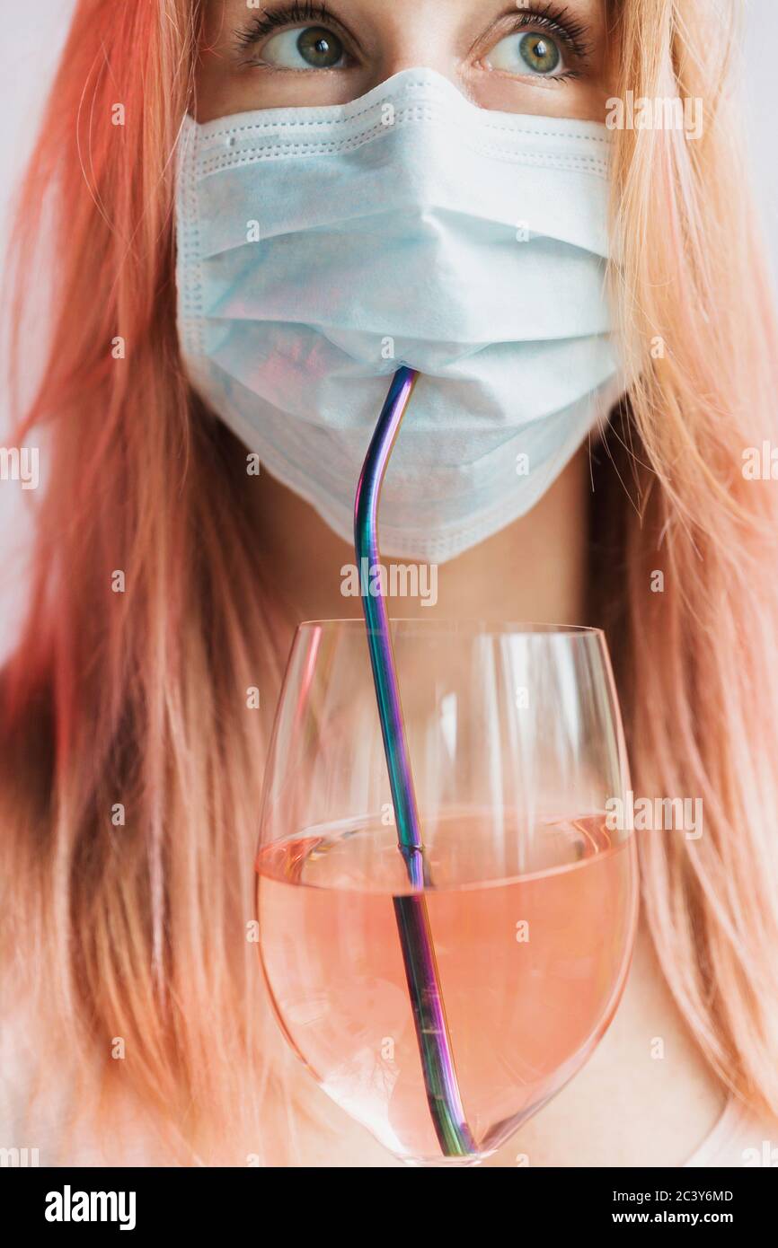 Woman drinking rose wine through straw while wearing face mask Stock Photo